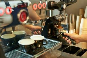 Close up of barista hand and coffee machine with fresh grinded beans, work in cafe photo