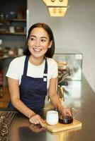 Vertical shot of smiling girl barista serving coffee, making batch brew, filter for client in cafe, wearing blue apron behind counter photo