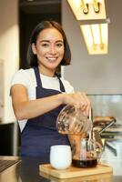 Vertical shot of smiling korean barista, pouring filter coffee, prepare batch brew for client in cafe, pour over method photo