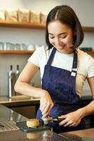 Vertical shot of barista, asian girl in cafe using tamper for coffee machine, wearing blue apron, preparing order photo