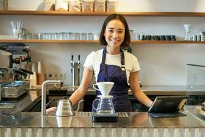 sonriente niña barista fabricación de cerveza filtrar café preparando orden en cafetería, en pie a mostrador foto