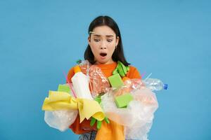 Shocked eco activist, collects loads of plastic to recycle, looking upset at bottles and unsorted garbage, blue background photo