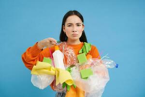 joven mujer muestra el plastico basura y pulgares abajo, no le gusta cuando personas son no reciclaje, azul antecedentes foto