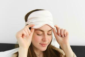 Smiling brunette woman open her eyes in morning, wake up in bed, take off sleeping mask, enjoying her bright start of the day, relaxing bedtime photo