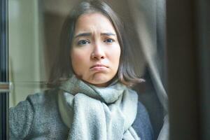 Portrait of sad ill woman staying at home, looking out of the window with jealous and upset face, cant leave home as being sick with covid-19 photo