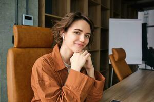 Close up portrait of young female entrepreneur, saleswoman in casual clothes, sitting in her office at the table and smiling photo