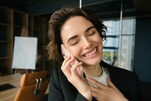 Close up portrait of happy woman in her office. Businesswoman answering a phone call with cheerful smile, receives great news over the telephone photo