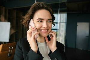 Close up portrait of happy woman in her office. Businesswoman answering a phone call with cheerful smile, receives great news over the telephone photo