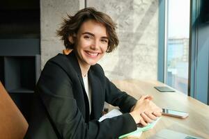 Young woman working in corporate, studying the case in her office, sitting in front of computer in black suit photo