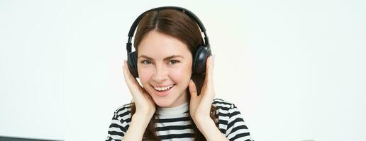 retrato de mujer, sonriente, vistiendo inalámbrico auriculares, escuchando música, estudiando en auriculares, en pie aislado terminado blanco antecedentes foto