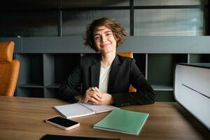 Portrait of young businesswoman working in her office, reading papers, studying documents of case and smiling, sitting in suit, having an interview photo