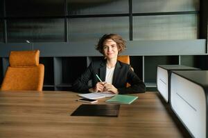 Portrait of saleswoman, business woman in office, sitting on chair with documents, reading papers, having an interview photo