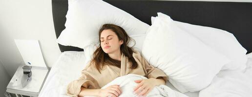 Top view of gorgeous woman in pyjamas sleeping, resting in bed with closed eyes, relaxing in hotel room photo