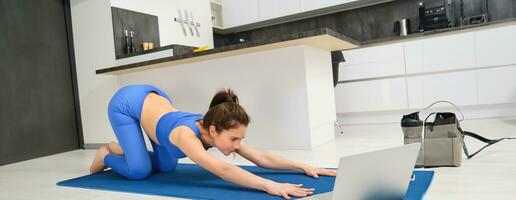 Image of young sportswoman, fitness girl watching online yoga tutorial on laptop and exercising, following video instructions photo