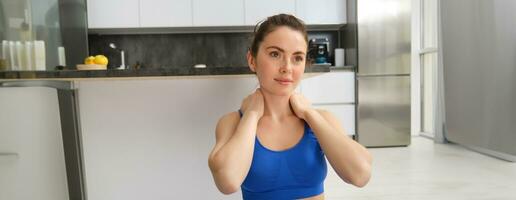 Close-up potrait of fitness woman, does training, workout from home, massaging neck, exercise in living room photo