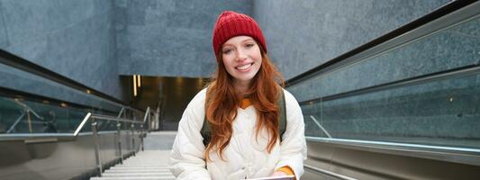 Beautiful redhead female model posing in city, walking up stairs with digital tablet, using gadget to plan her route, reading while going somewere photo