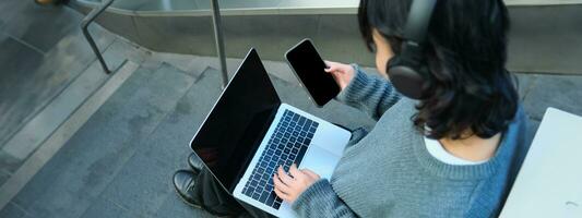 Close up portrait of girl, student works on laptop and listens music in headphones. Blank computer screen and hands typing on keyboard photo