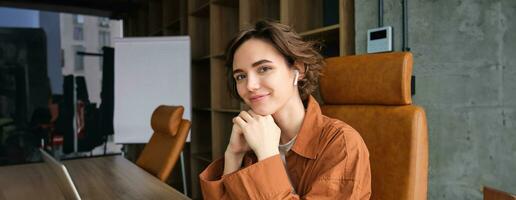 Close up portrait of young female entrepreneur, saleswoman in casual clothes, sitting in her office at the table and smiling photo