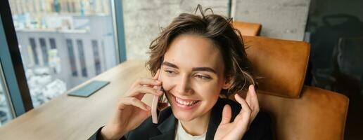 imagen de exitoso mujer hablando en móvil teléfono, teniendo un conversacion terminado el teléfono, respondiendo cliente, sentado y trabajando en un oficina foto