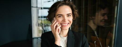 Portrait of successful businesswoman making calls, standing in office and talking with client photo