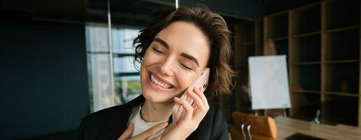 Close up portrait of happy woman in her office. Businesswoman answering a phone call with cheerful smile, receives great news over the telephone photo