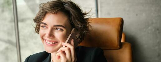 Close up portrait of corporate woman laughing and smiling, talking over the phone, sitting in office photo