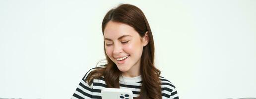 Portrait of girl with smartphone laughing, using mobile phone app, isolated on white background photo