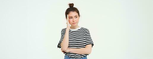 Portrait of concerned, worried young woman, touches her head, looking complicated, standing over white background photo