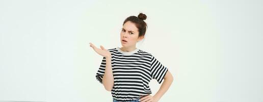 Portrait of angry woman complaining, raising one hand and shrugging looking frustrated, waiting for explanation, doesnt udnerstand smth, standing over white background photo