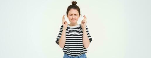 Nervous girl, student cross fingers for good luck, making wish, hoping for something, anticipating positive results, standing over white background photo