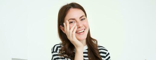 Lifestyle. Happy young woman laughing, touching her face and smiling at camera, white background photo