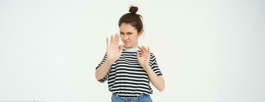 Image of woman refusing something, raising hands in defensive gesture, protecting herself, rejecting offer, declining, standing over white background photo