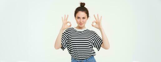 No problem, excellent choice. Smiling, confident young woman, showing okay, ok sign, zero gesture, recommends product, stands over white background photo