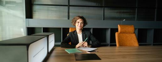 Portrait of saleswoman, business woman in office, sitting on chair with documents, reading papers, having an interview photo