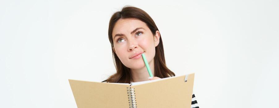 retrato de estudiante haciendo su tarea, participación cuaderno y bolígrafo, pensando mientras haciendo notas en su computadora portátil, en pie terminado blanco antecedentes foto
