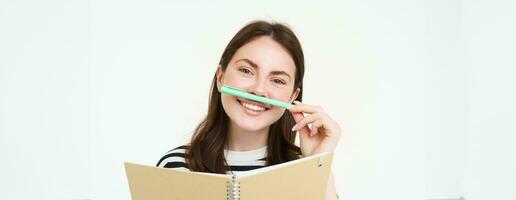 retrato de divertido, sonriente mujer con computadora portátil, participación bolígrafo siguiente a su labio y mirando feliz, blanco antecedentes foto