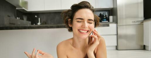 Close up portrait of happy smiling woman talking on mobile phone from her kitchen. Chatty girl with smartphone, laughing, calling someone photo