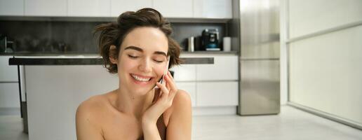 Close up portrait of happy smiling woman talking on mobile phone from her kitchen. Chatty girl with smartphone, laughing, calling someone photo