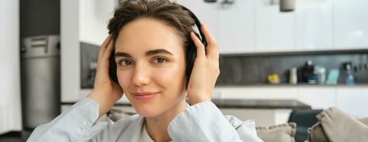 Close up portrait of woman enjoying listening to music in headphones, sitting at home on sofa with earphones on head photo