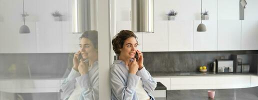 Portrait of cute young woman answers a phone call, talks on smartphone, spends time at home photo