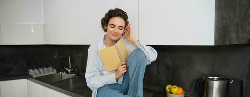retrato de sonriente joven mujer leyendo diario, disfruta comodidad a hogar, participación computadora portátil, mirando feliz, relajante adentro foto