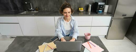 hermosa Trabajadores por cuenta propia niña trabajos desde hogar. joven mujer en línea estudiando, acecho curso en sitio web, mirando a ordenador portátil pantalla foto