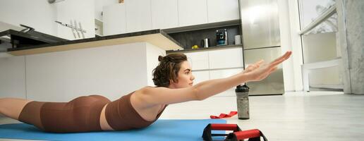 Portrait of sportswoman at home, doing workout training, stretching arms forward, leading active lifestyle from indoors, using resistance band and plunk push up bars for exercising photo