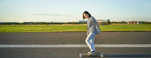 Beautiful asian skater girl riding her longboard on sunny empty road. Young woman enjoying her skate ride smiling and laughing photo