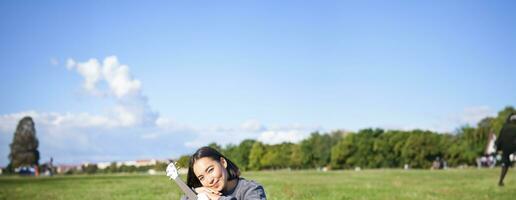 Romantic asian girl sitting with ukulele guitar in park and smiling, relaxing after university, enjoying day off on fresh air photo