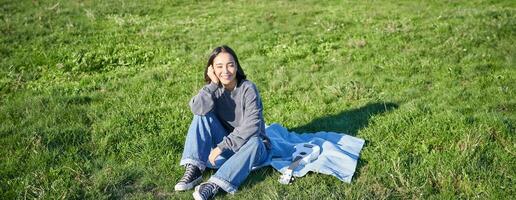 Young asian girl enjoying sunny day outdoors. Happy student having picnic on grass in park, playing ukulele photo