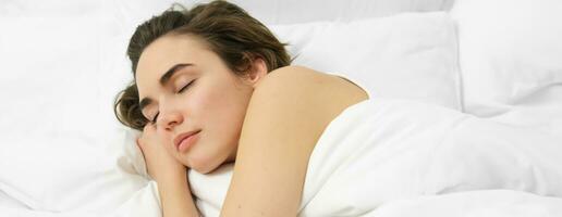 Woman lying asleep in her bed, eyes closed, face is calm and relaxed, hugging soft, comfortable pillow photo