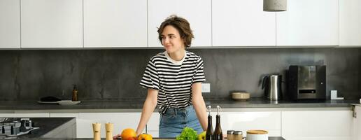 Portrait of smiling cute young woman making breakfast, chopping vegetables in the kitchen, preparing vegan meal photo