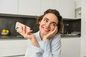 Portrait of woman thinking while holding smartphone, deciding what to order on mobile phone app photo