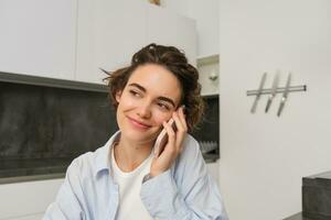 Image of woman working at home, making a phone call, sitting with smartphone, surrounded with paperwork, doing homework and talking to someone photo